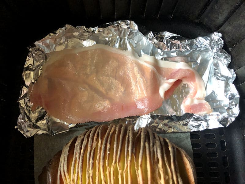 Hasselback potato with bacon rasher positioned in foil inside air fryer