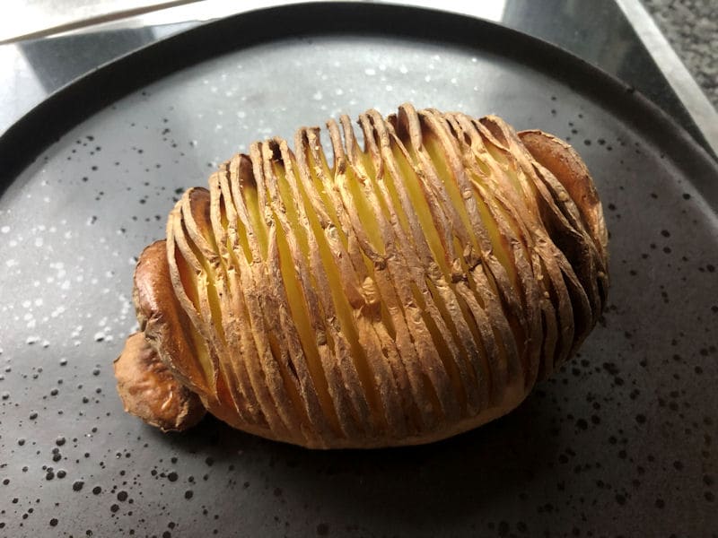 Cooked Hasselback potato sat on centre of matte black dinner plate