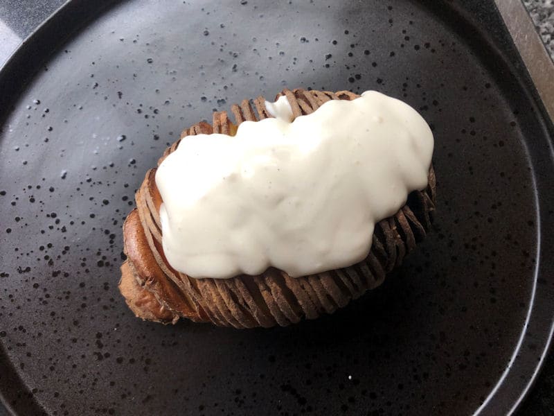 Hasselback potato positioned on plate with dressing spooned on top