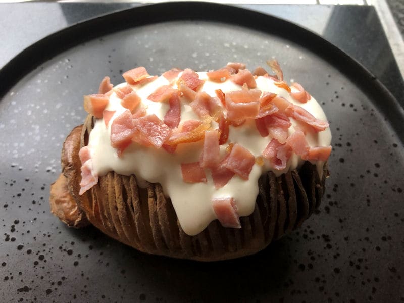 Hasselback potato on plate with dressing and bacon bits on top