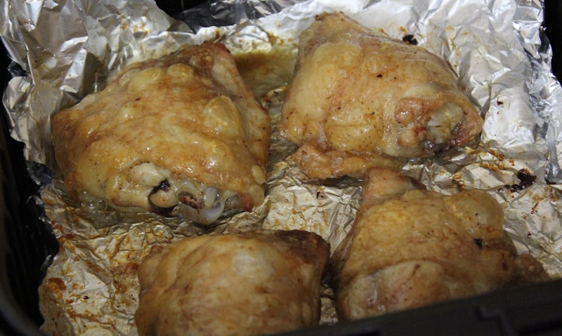 Four cooked skin-on crispy chicken thighs sitting on foil in air fryer basket