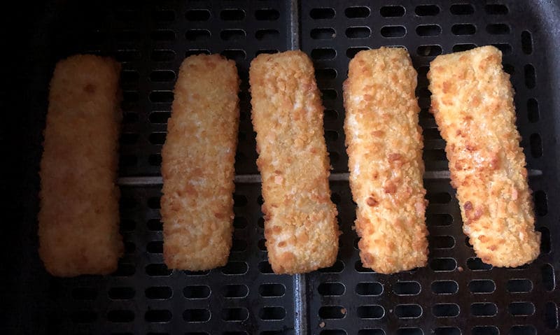 Five Birds Eye breaded fish fingers positioned in a row in air fryer basket