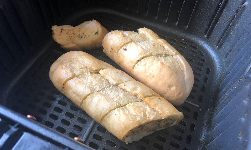 Cut in half standard size garlic baguette sitting in air fryer basket