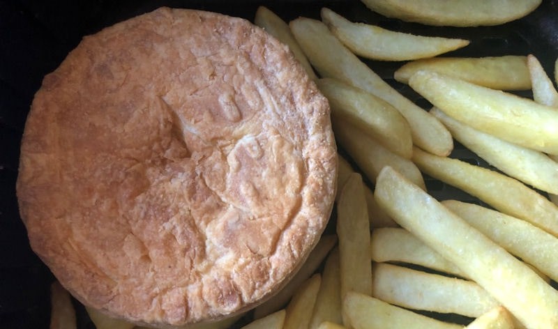 Cooked steak and potato pie and frozen chips in air fryer basket