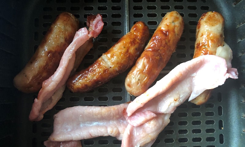 Pork sausages and back bacon cooking together in air fryer basket