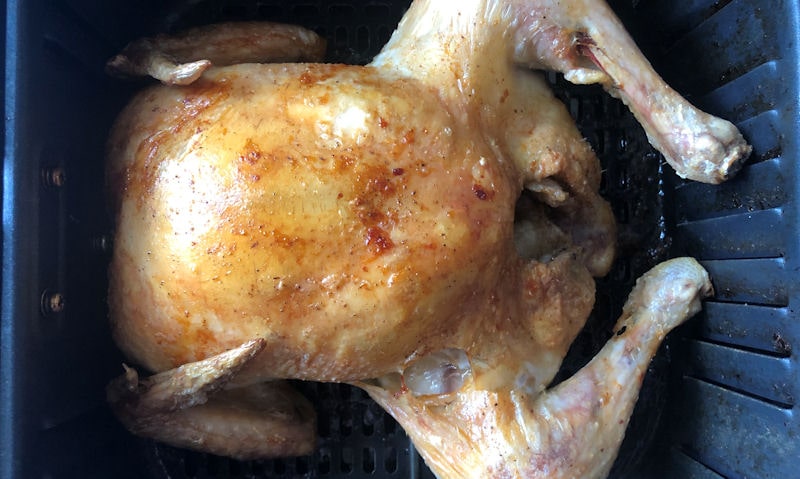 Partially cooked whole small chicken sitting in air fryer basket