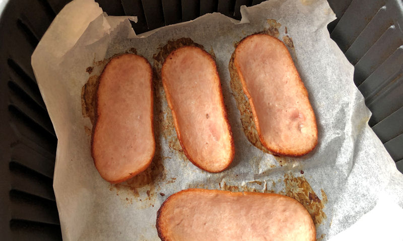 Cooked turkey bacon sat in air fryer basket, on parchment paper