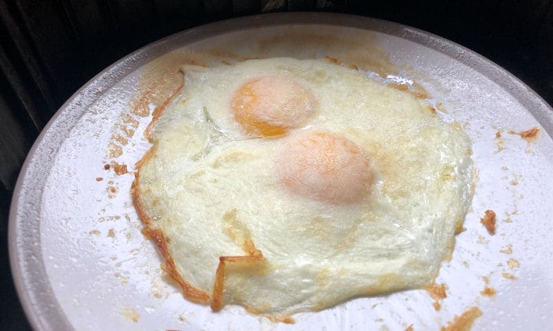 Air fried eggs cooked on small ceramic plate inside air fryer basket