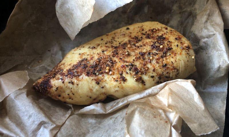 Reheated chicken breast visible amongst baking paper wrapper in air fryer