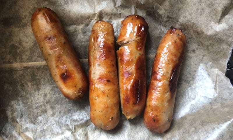 Four air fryer reheated pork sausages on parchment paper