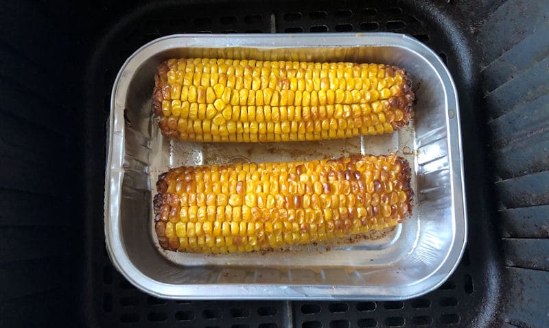 Fully roasted corn on the cobs in foil tray positioned in air fryer basket