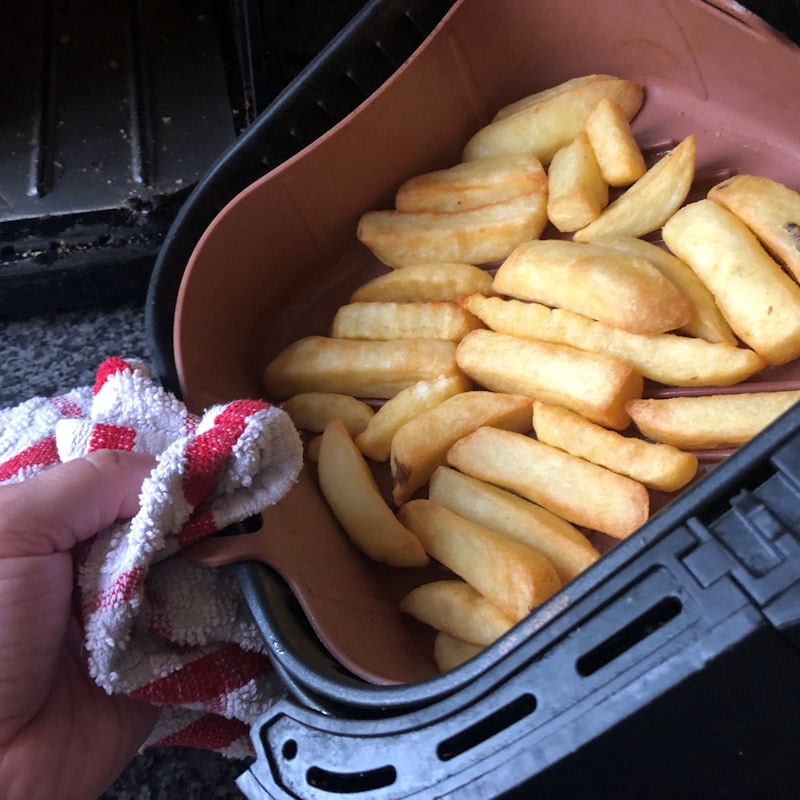 Pulling silicone basket out of air fryer basket with kitchen towel