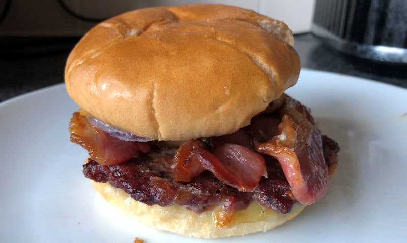 Reheated burger in a bun sitting on countertop on a plate