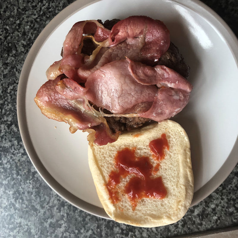 Open face hamburger with bun sitting on plate with bacon on top