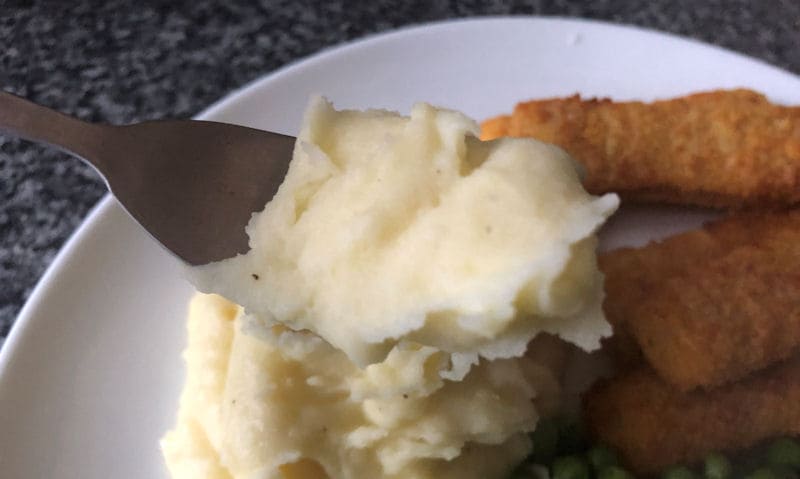 Air fried mashed potatoes on fork with fish fingers and peas on plate