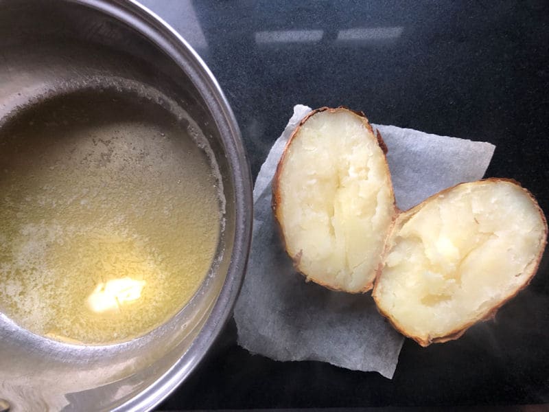 Air fried baked potato cut in half next to saucepan of melted butter