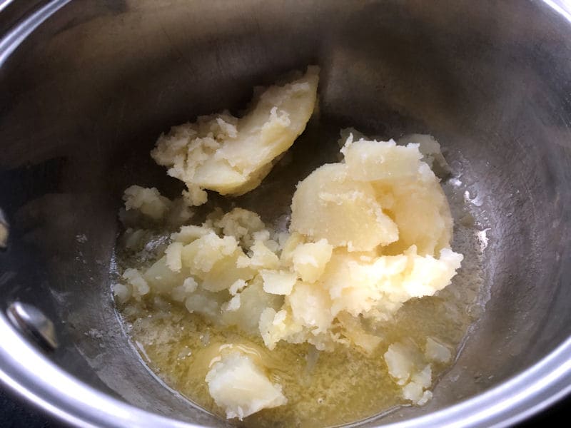 Soft potato flesh spooned into saucepan of melted butter