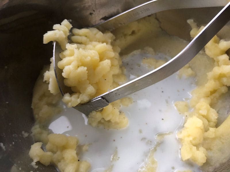 Forkful of mashed potato served with peas and fish fingers