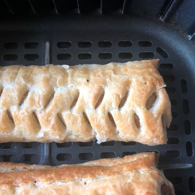 Cold soft pale puff pastry sausage rolls sitting in air fryer basket