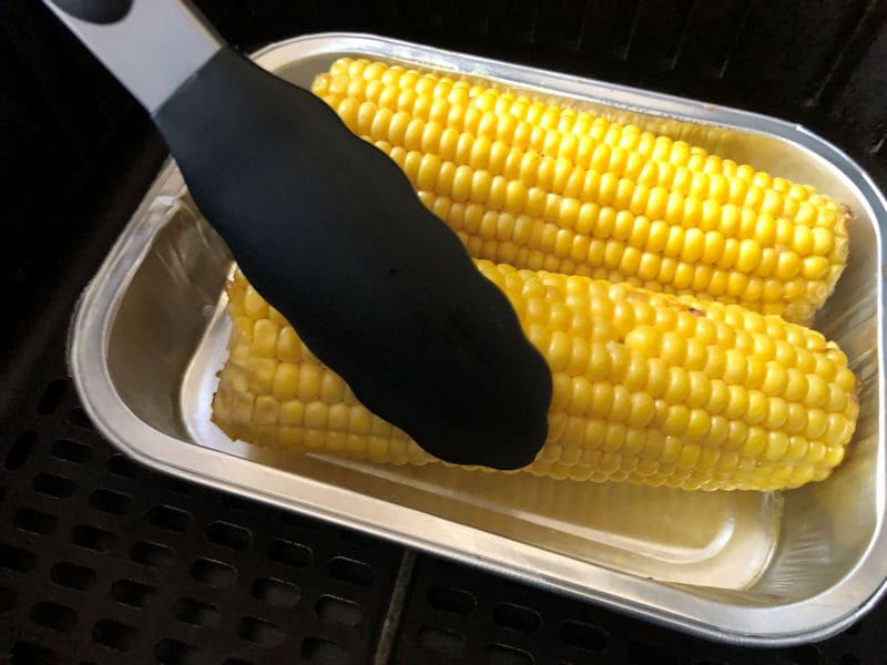 Rotating corn on the cob with tongs in air fryer basket