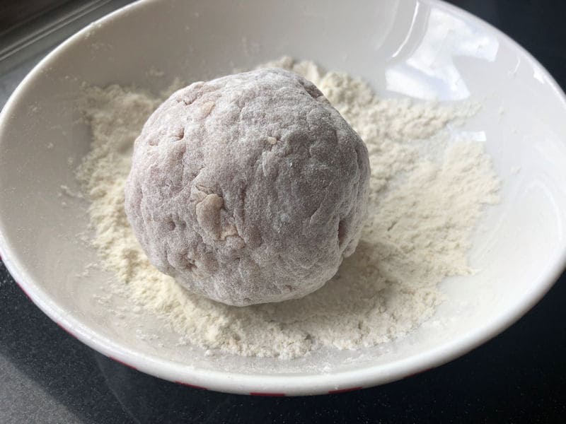 Single raw Scotch Egg coated in light dusting of flour in plastic bowl