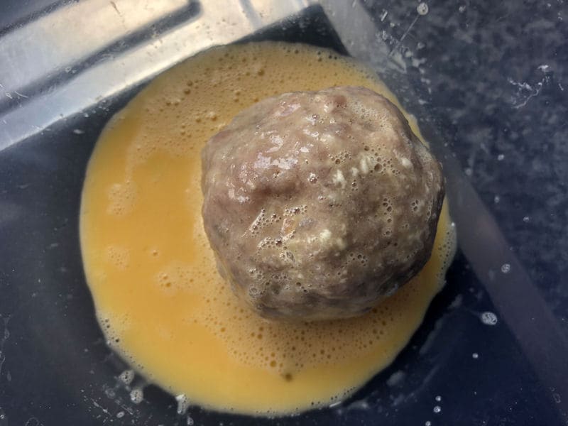 Flour coated raw Scotch Egg covered in beaten egg in plastic bowl