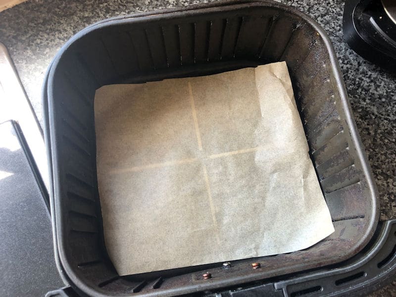 Square sheet of parchment paper covering bottom of air fryer basket