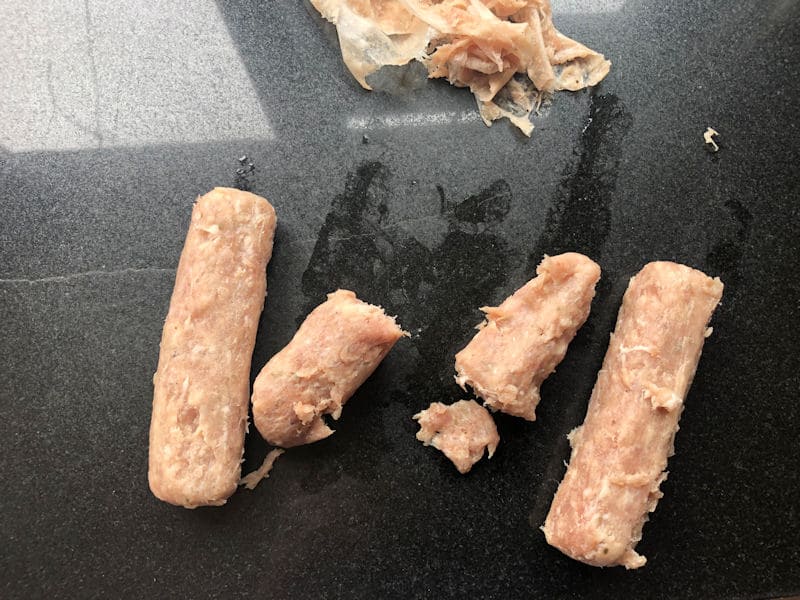 Raw sausages with casing cut off; casing peel near by on chopping board