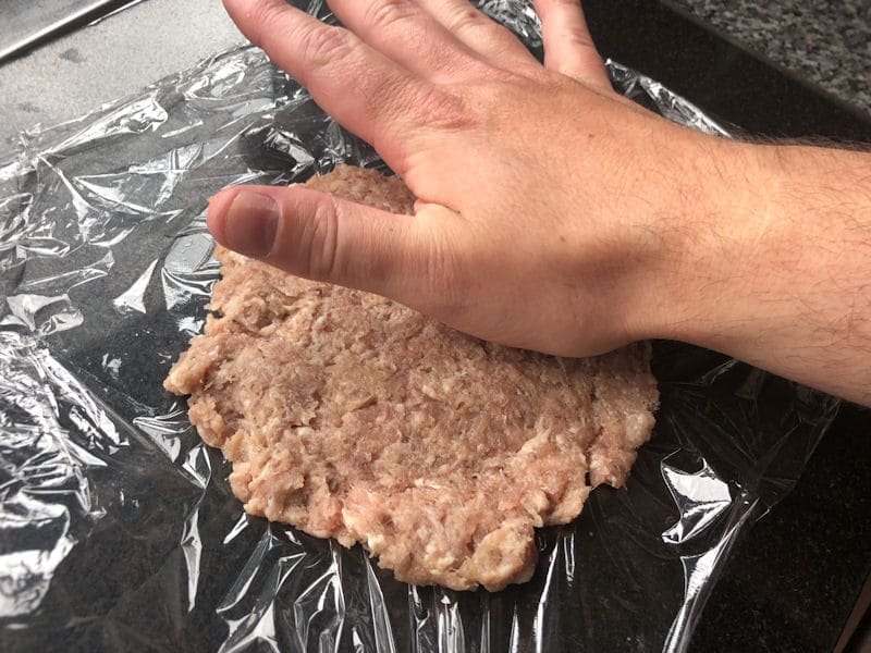 Pressing flat sausage balls into patties on clingfilm