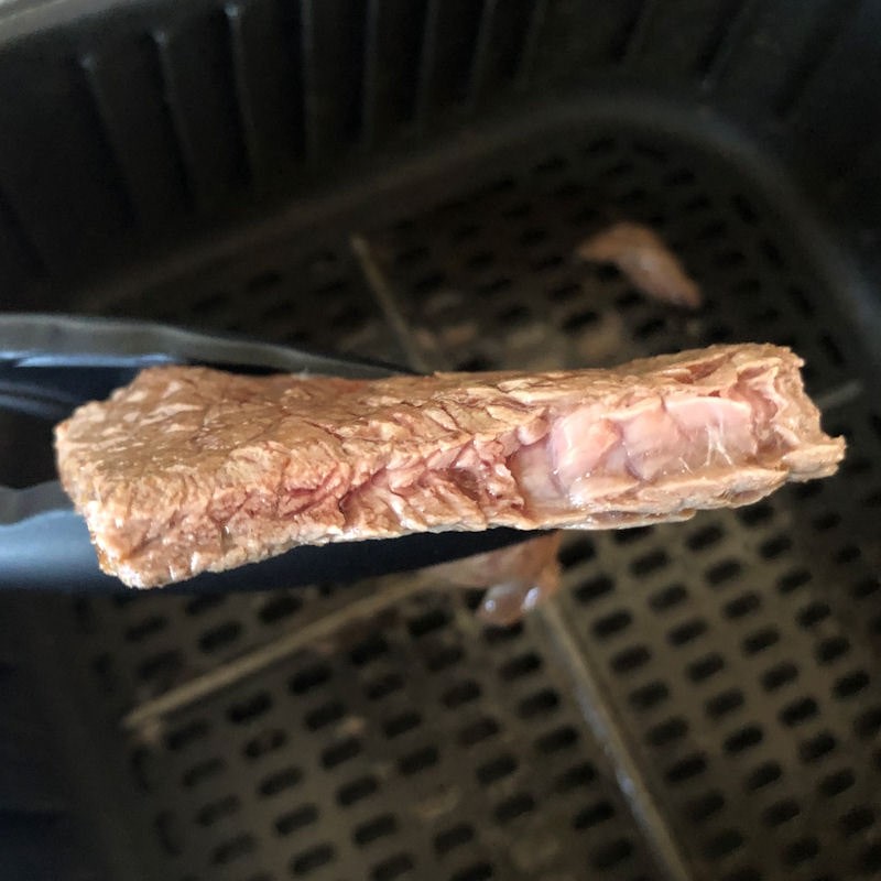 Cut open medium rare sizzle steak held in tongs