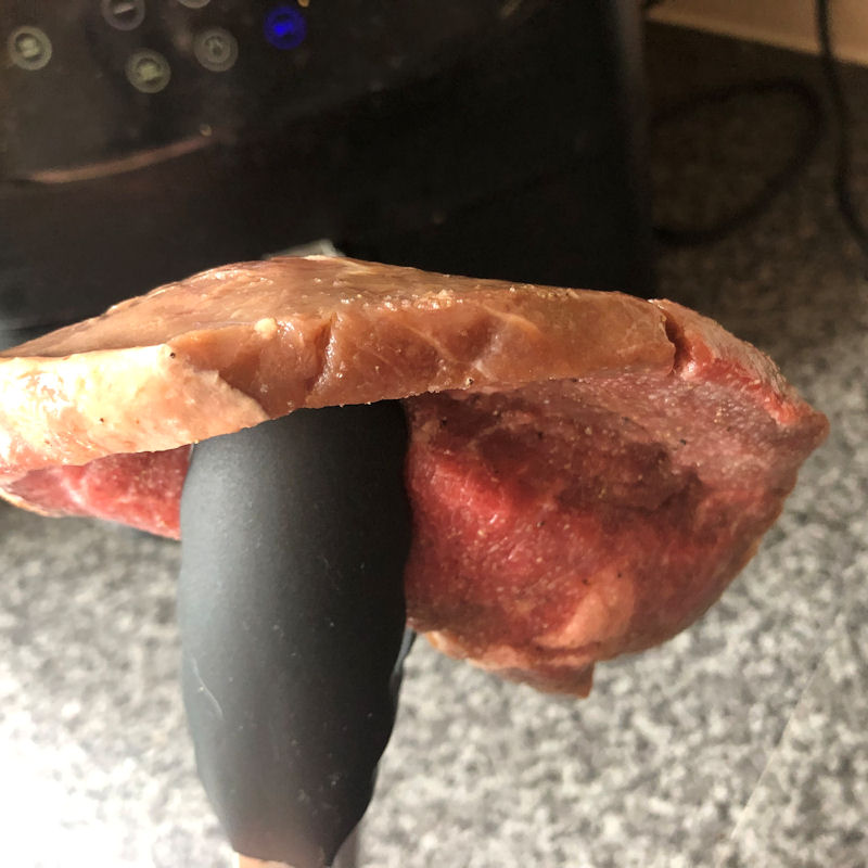 Sizzle Steak held in tongs to demonstrate thickness