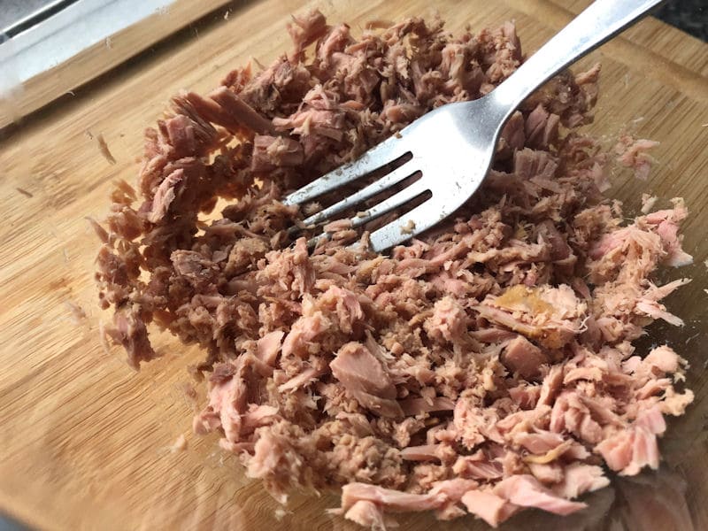 In process of breaking down tuna chunks in glass bowl with fork