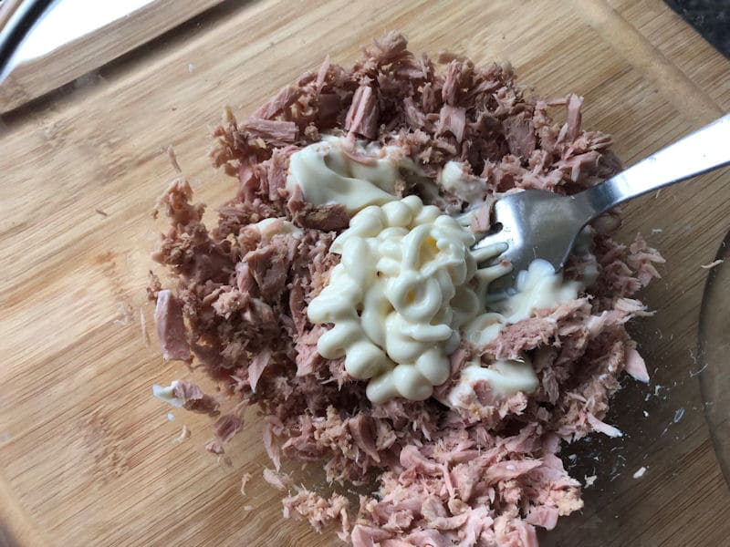 Spoonfuls of mayonnaise settled on top of tuna chunks in glass dish