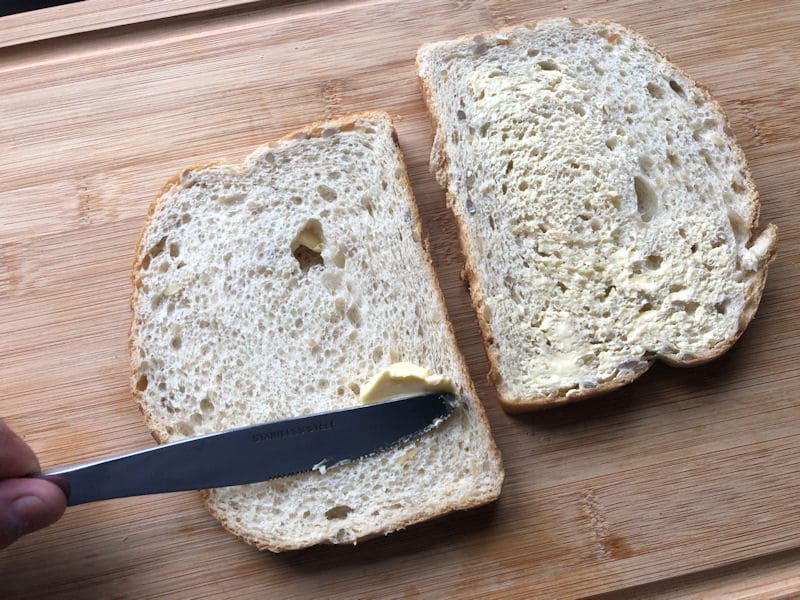 In process of buttering second slice of bread on chopping board