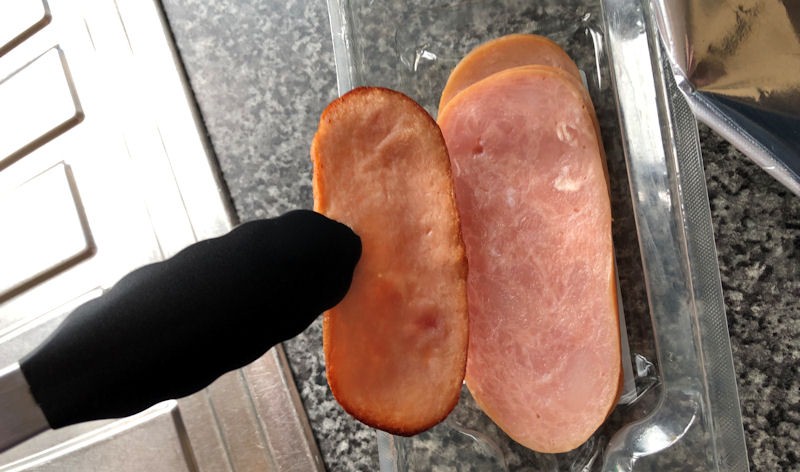 Holding shrunk cooked turkey bacon next to uncooked original size turkey bacon in package